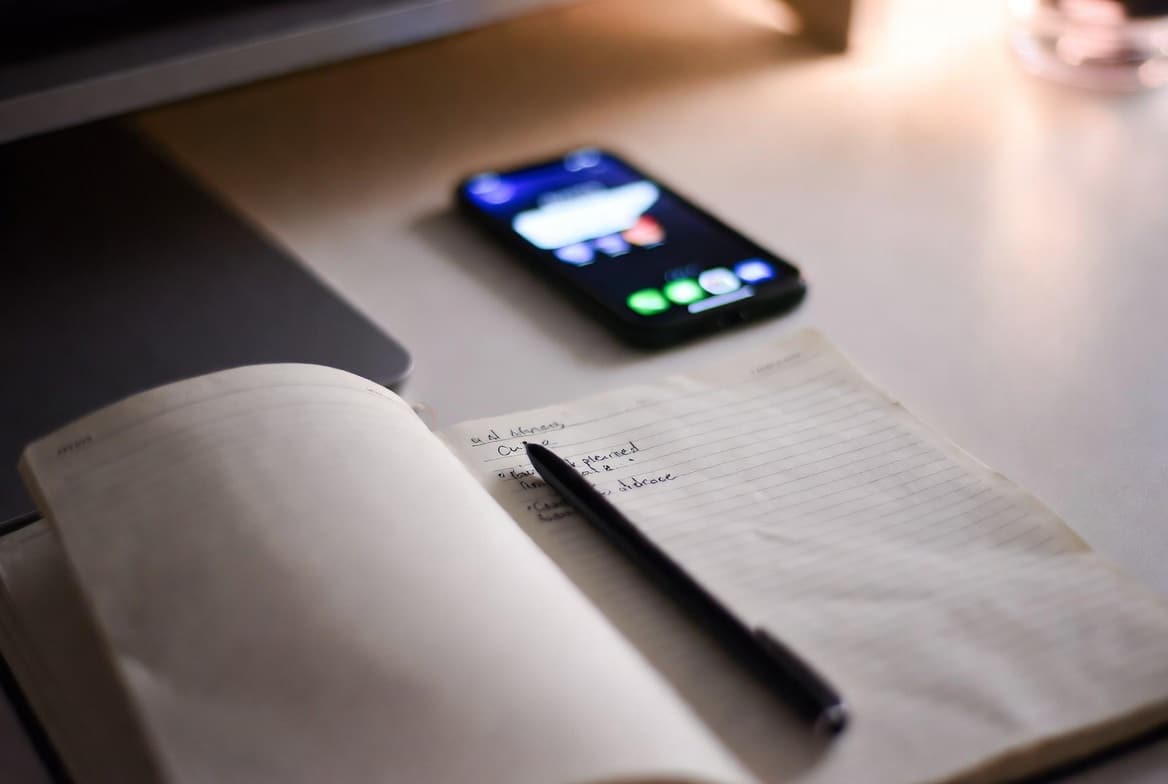 Caderno manuscrito em foco sobre mesa de trabalho e celular com notificação de aplicativo ignorado ao lado